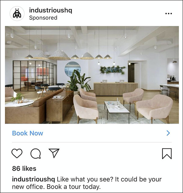 Annuncio Instagram di IndustriousHQ con una foto di uno dei loro uffici moderni con pareti bianche e accenti di legno chiaro con didascalia, 