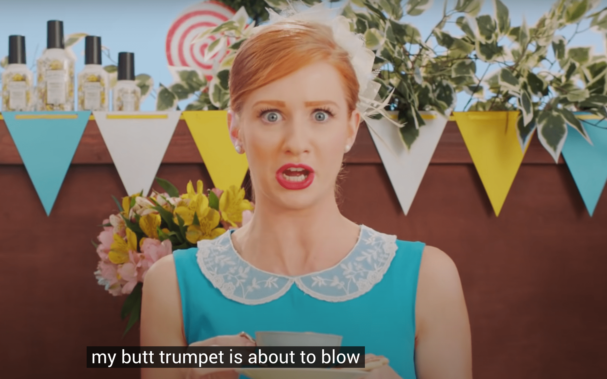 spot pubblicitari di poopourri con una giovane donna dai capelli rossi in un abito da festa blu.  Il testo dice: La mia tromba del culo sta per suonare.